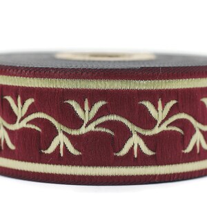 Op de afbeelding: Een close-up van een bordeauxrood lint met een gouden bloemenontwerp. Het lint heeft een textuur en is perfect om een ​​toets van elegantie aan elk project toe te voegen.