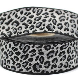 May include: Black and gray leopard print ribbon with a black border. The ribbon is rolled up and the print is visible on both sides.