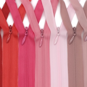 May include: Assortment of eight zipper tapes in various shades of red and pink. The zippers are laid out in a criss-cross pattern.