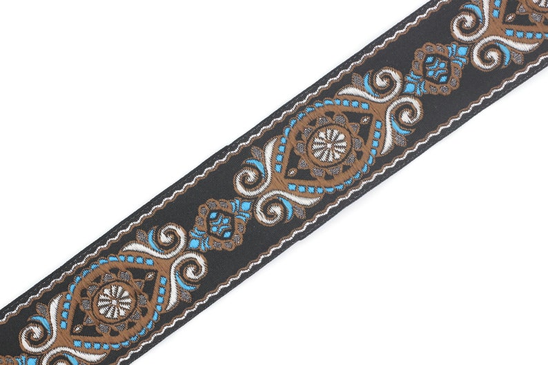 May include: Black woven trim with a white and brown paisley design. The trim features a repeating pattern of stylized floral motifs and swirls.