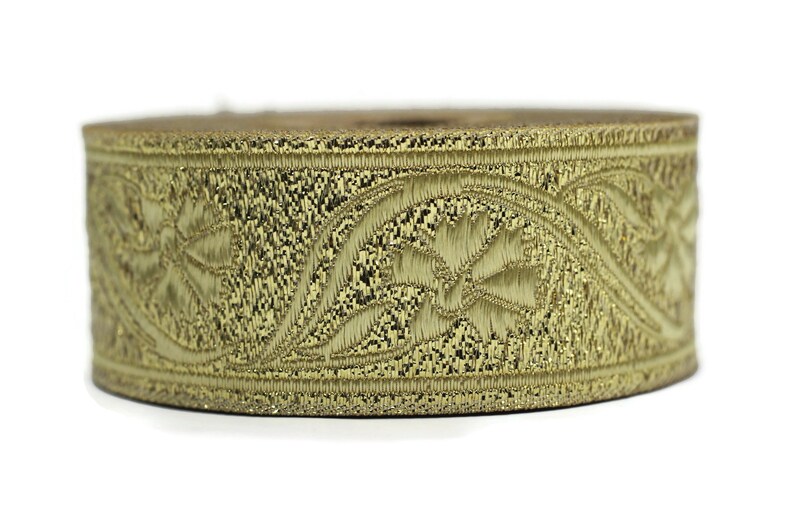 May include: A spool of gold-colored embroidered trim. The trim features a repeating floral and leaf pattern. The trim is likely made of a metallic thread, giving it a shiny appearance. The trim is suitable for sewing and crafting projects.