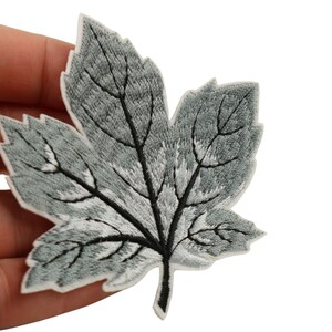 May include: A gray embroidered iron-on patch of a maple leaf with a white outline.