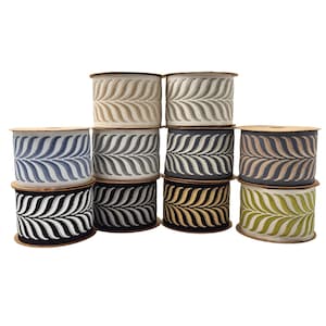 May include: A collection of decorative ribbon spools in various colors, including blue, gray, black, and gold. Each spool features a repeating leaf-like pattern in a contrasting color. The spools are stacked and arranged against a white background.