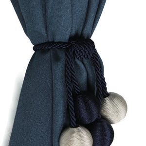 Pode incluir: Uma cortina azul escura com um cordão de amarração azul marinho e bolas decorativas. As bolas são uma mistura de azul marinho e bege claro.