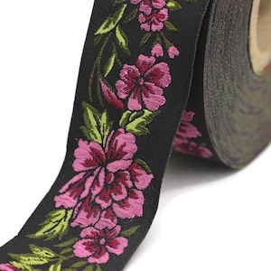 Puede incluir: Cinta negra con bordado floral rosa y verde. La cinta est&aacute; enrollada y el dise&ntilde;o floral es visible.