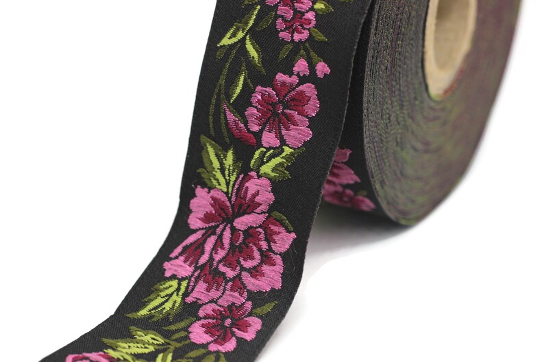 Puede incluir: Cinta negra con bordado floral rosa y verde. La cinta est&aacute; enrollada y el dise&ntilde;o floral es visible.