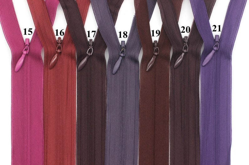 May include: Seven different colors of zipper tape, numbered 15 through 21. The zipper tape is a thin, flexible material with a subtle ribbed texture. The colors are pink, red, brown, purple, dark brown, light brown, and purple.