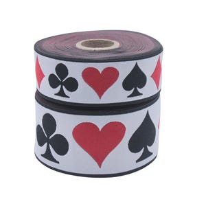 May include: A roll of white elastic with a black and red repeating pattern of playing card suits. The suits are hearts, spades, clubs, and diamonds.