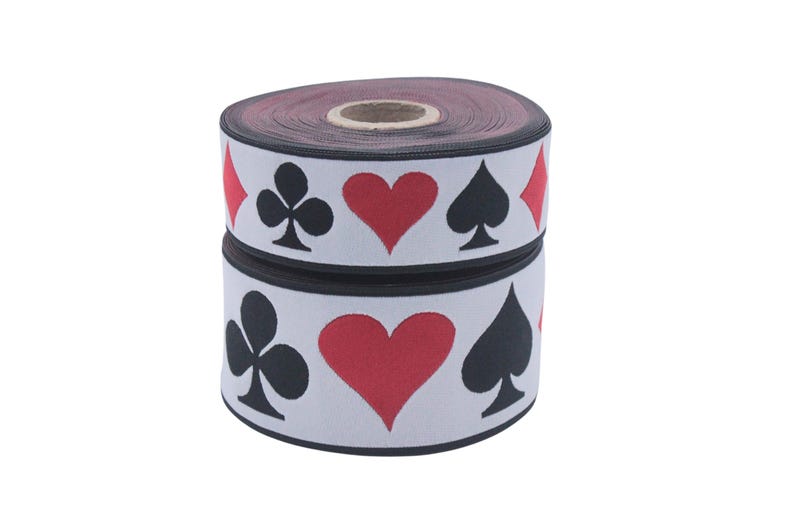 May include: A roll of white elastic with a black and red repeating pattern of playing card suits. The suits are hearts, spades, clubs, and diamonds.
