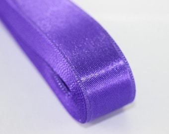 May include: A roll of purple satin ribbon. The ribbon is folded in half and the edges are visible.