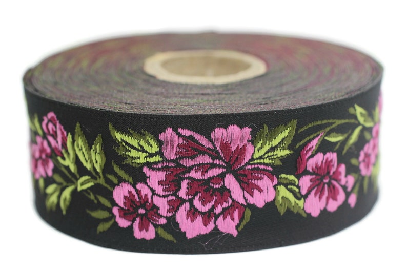 Puede incluir: Un rollo de cinta negra con un patr&oacute;n floral. La cinta est&aacute; decorada con flores bordadas de color rosa y verde.