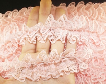 May include: Pink ruffled lace trim with a delicate floral pattern. The lace is soft and flowing, making it perfect for adding a touch of elegance to any project.