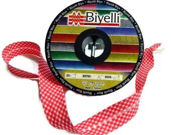 Könnte beinhalten: Eine Spule mit rot-weißem Gingham-Band mit einem Etikett, auf dem "Biyelli" und "Made in Türkiye" steht. Das Etikett enthält auch Waschanweisungen und den Text "EN: 1 METRE: 25 RENK: 64".