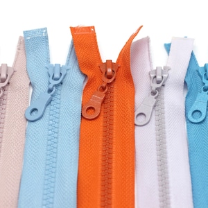 May include: A close-up of eight different colored zippers, including pink, light blue, orange, white, blue, and navy blue.