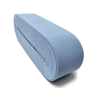 May include: A roll of light blue elastic band material. The elastic is tightly wound, revealing the layered texture of the fabric. The color is a soft, muted blue, suitable for various sewing and crafting projects.