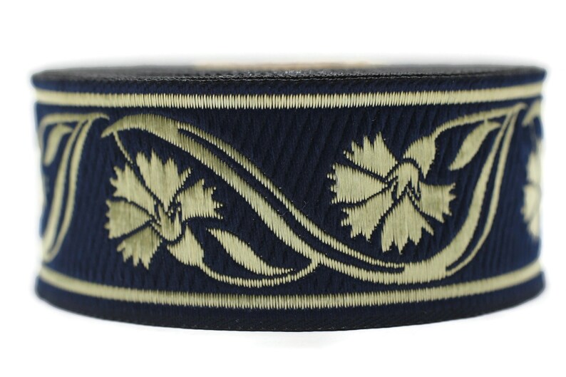 May include: A navy blue hat with an embroidered floral design in a light gold color. The hat features a black band at the top and bottom, and the floral pattern wraps around the hat's circumference.