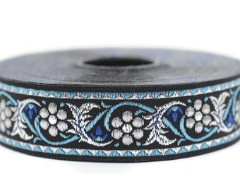 Puede incluir: Un rollo de ribete negro con un patrón floral plateado y azul. El ribete tiene un diseño repetitivo de flores y hojas estilizadas.