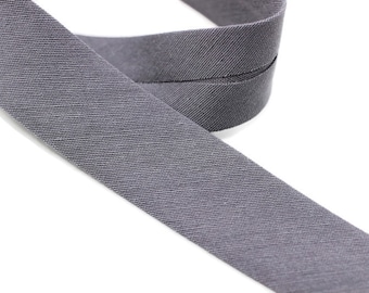 May include: Gray cotton twill tape with a zig-zag stitch down the center. The tape is folded in half and the ends are overlapping.