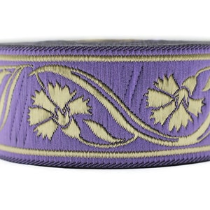 May include: A roll of decorative ribbon featuring a floral design. The ribbon has a lavender background with gold-colored embroidered flowers and accents. The edges are dark purple.
