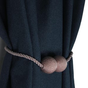 May include: A dark blue curtain with a brown rope tieback featuring two round decorative balls.