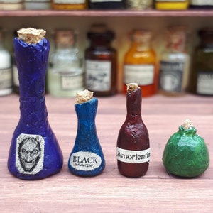 Puede incluir: Una colección de botellas de pociones en miniatura con tapones de corcho. Las botellas son de varios colores, incluyendo azul, rojo y verde, y presentan etiquetas con texto e imágenes. Las botellas están dispuestas sobre una superficie rosa.