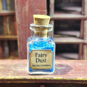 Puede incluir: Una pequeña botella de vidrio llena de purpurina azul, etiquetada como "Fairy Dust". La botella tiene un tapón de corcho y una etiqueta rectangular con el texto en una fuente vintage. El fondo incluye una estantería de madera y libros.