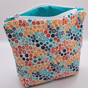 May include: A white zippered pouch with a turquoise lining. The pouch is covered in a floral pattern with small orange, blue, and black flowers on a white background.