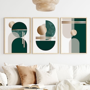 Könnte beinhalten: Drei gerahmte abstrakte Kunstdrucke. Jeder Druck zeigt geometrische Formen in Grün-, Beige- und Goldtönen. Die Kunstwerke werden über einem weißen Sofa mit neutralfarbenen Wurfkissen und einem Holztisch ausgestellt, wodurch eine moderne Wohnzimmerästhetik entsteht.