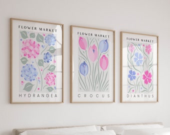 May include: Three framed prints with a white background and a floral design. Each print has the text "FLOWER MARKET" at the top and the name of a flower at the bottom. The flowers are hydrangea, crocus, and dianthus.