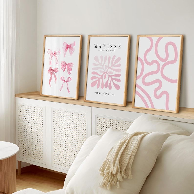 K&ouml;nnte beinhalten: Drei gerahmte Drucke mit rosafarbenen abstrakten Designs. Der linke Druck zeigt rosafarbene Schleifen, der mittlere Druck hat ein rosafarbenes Blumenmuster mit dem Text "MATISSE PAPIERS DECOUPES BERGGREN & CIE", und der rechte Druck hat ein rosafarbenes abstraktes Design.