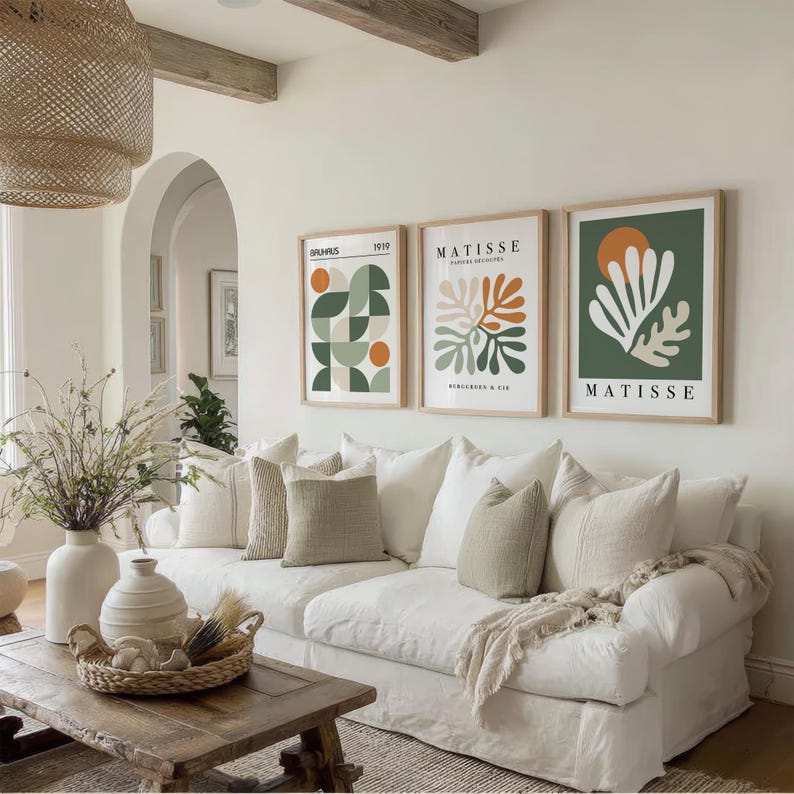 May include: A living room with a white sofa, decorative pillows, and a wooden coffee table. Three framed Matisse art prints hang above the sofa. A woven pendant light and vases with dried plants add to the room's decor.