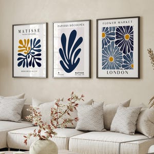 Puede incluir: Tres impresiones de arte enmarcadas con un dise&ntilde;o minimalista. Las impresiones presentan patrones florales abstractos en tonos de azul y amarillo. El texto en las impresiones dice "Matisse, Papiers Decoupes, Flower Market, London y Bergcren & Cie."