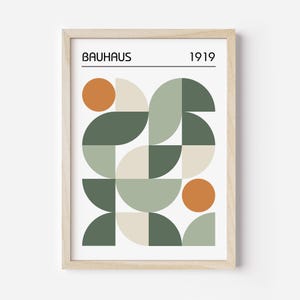 May include: Framed Bauhaus art print featuring a geometric design in shades of green, beige, and orange. The print includes the word "BAUHAUS" and the year "1919" in a minimalist font, set against a white background.
