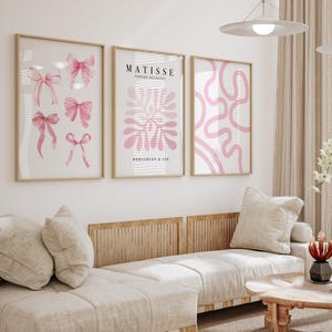 K&ouml;nnte beinhalten: Drei gerahmte Kunstdrucke mit rosafarbenen abstrakten Designs. Der mittlere Druck zeigt den Text "MATISSE PAPIERS DECOUPES BERGGREN & C:IE".