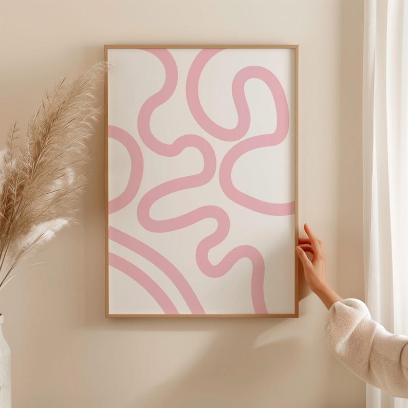 K&ouml;nnte beinhalten: Ein gerahmter abstrakter Druck mit einem rosa und wei&szlig;en Design. Der Druck zeigt eine Reihe von rosa Linien, die ein wirbelndes, organisches Muster erzeugen.