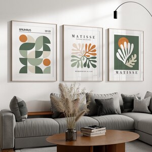 May include: Three framed art prints with abstract designs. The prints feature geometric shapes and botanical illustrations in shades of green, orange, and beige. The text "BAUHAUS 1919" and "MATISSE PAPIERS D&Eacute;COUP&Eacute;S" are visible.