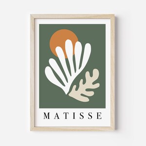 May include: A framed art print featuring a minimalist design. The artwork showcases white and beige organic shapes against a dark green background, with an orange circle resembling a sun. The word "MATISSE" is printed in black at the bottom.
