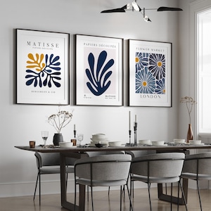 Puede incluir: Tres impresiones de arte enmarcadas con un dise&ntilde;o minimalista. Las impresiones presentan formas abstractas en azul y amarillo sobre un fondo blanco. El texto en las impresiones dice "Matisse, Papiers Decoupes, Flower Market, London".