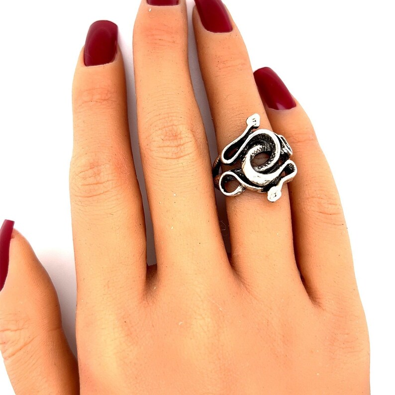 K&ouml;nnte beinhalten: Silberner Schlangenring mit einem gewundenen Design. Der Ring wird an einer Hand mit rotem Nagellack getragen.