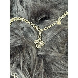 May include: Silver-toned necklace with a clover-shaped pendant. The pendant has four heart-shaped designs, each with a small, clear stone. The chain is made of small, oval links and has a clasp closure.