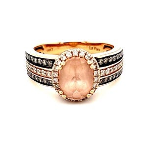 May include: A rose gold ring with a large oval-shaped pink gemstone surrounded by a halo of smaller diamonds. The band is adorned with three rows of alternating diamonds and black diamonds.