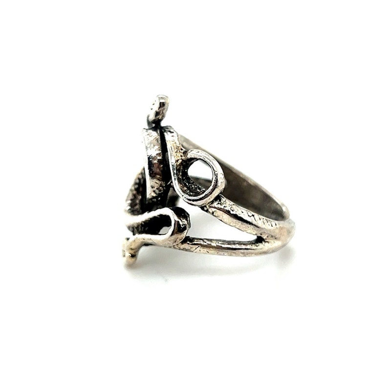 K&ouml;nnte beinhalten: Ein silberner Ring mit einem komplizierten Design, das ein Spiralmuster und einen herzf&ouml;rmigen Ausschnitt aufweist. Der Ring ist aus strukturiertem Metall gefertigt und hat einen einzigartigen, organischen Look.