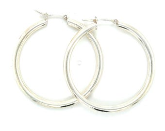 May include: A pair of silver hoop earrings. The earrings are round and have a polished finish. The hoops are of medium thickness and have a simple, classic design. The earrings are displayed against a white background.