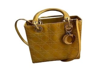 May include: A yellow leather handbag with a gold-tone chain strap and a gold-tone charm. The bag has a quilted design and a top zipper closure.
