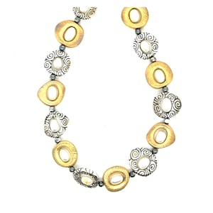 Puede incluir: Un collar con eslabones ovalados dorados y circulares plateados alternados. Los eslabones dorados tienen una abertura ovalada central, mientras que los eslabones plateados tienen un dise&ntilde;o en espiral. Peque&ntilde;as cuentas oscuras conectan los eslabones.