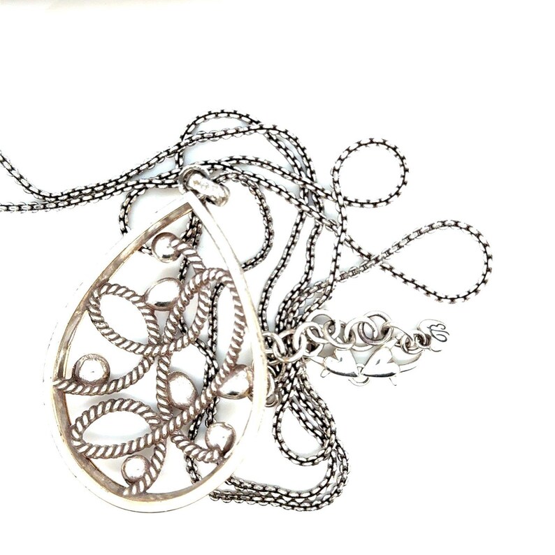 May include: Silver necklace with a teardrop pendant. The pendant has an openwork design of rope-like patterns and small circular accents. The chain is dark silver, and the clasp has heart-shaped details.
