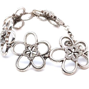 Pode incluir: Pulseira prateada com design floral. Cada flor tem cinco p&eacute;talas vazadas e um centro adornado com pequenos cristais transparentes. A pulseira &eacute; ligada com pequenos conectores circulares.