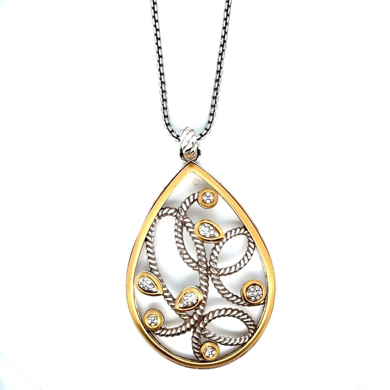 May include: A teardrop pendant necklace with a gold-tone frame and silver-tone interior. The pendant features a swirling rope design with clear gemstones. The necklace has a silver chain. The pendant is a statement piece.
