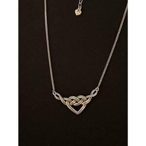 May include: Silver-toned necklace featuring a heart-shaped pendant with an interwoven knot design. The pendant is connected to a delicate chain, and the necklace has a small heart charm near the clasp. The jewelry is displayed against a black background.