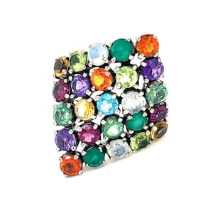 May include: A silver ring with a square-shaped setting featuring a cluster of colorful gemstones. The ring is set with a variety of stones, including amethyst, citrine, peridot, aquamarine, and topaz.